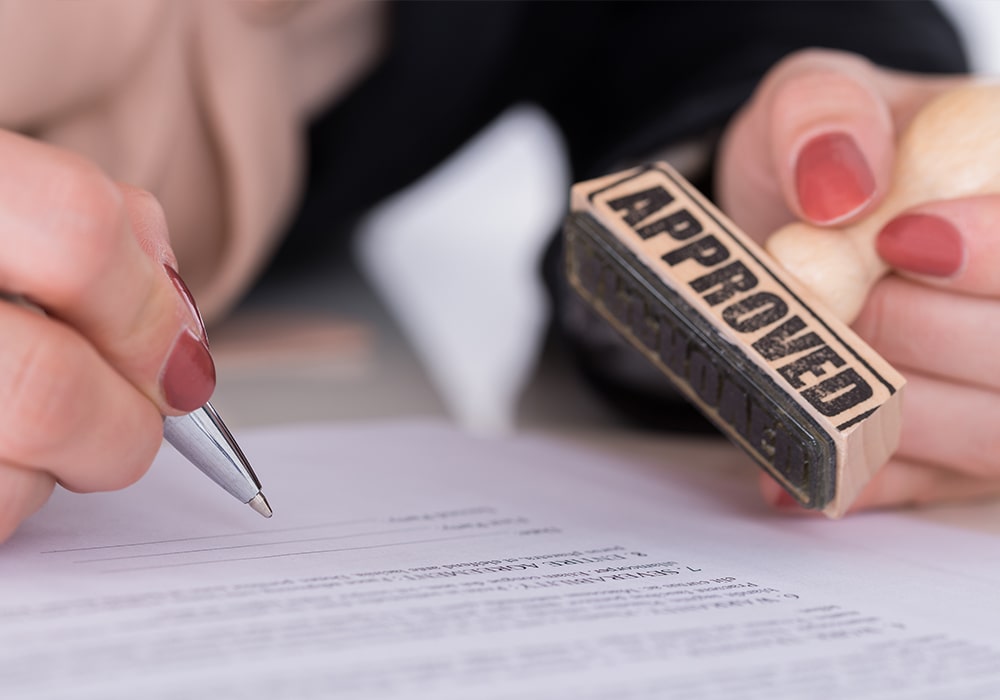 A woman's hand stamping documents with 'approved'.